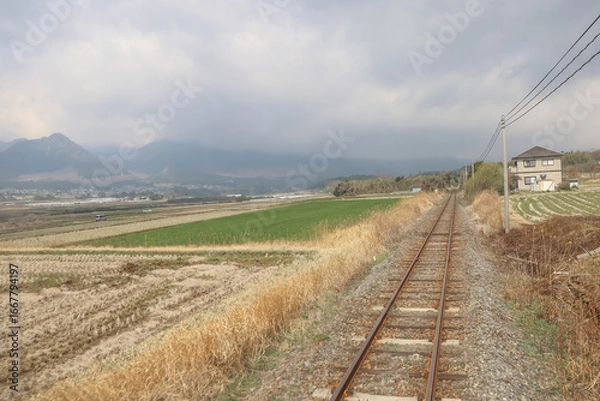 Obraz March 26 2025 Rural Railway Passing Through Scenic Countryside with Fields and Mountains, Japan
