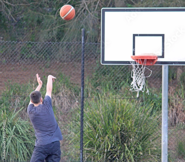 Fototapeta A man throwing a basketball into a hoop. Practicing basketball
