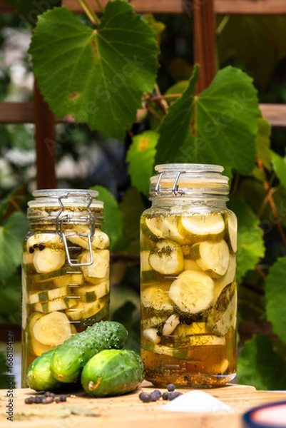 Fototapeta Dill pickles in a glass jar on a table in an outdoor garden. Vertical shot.