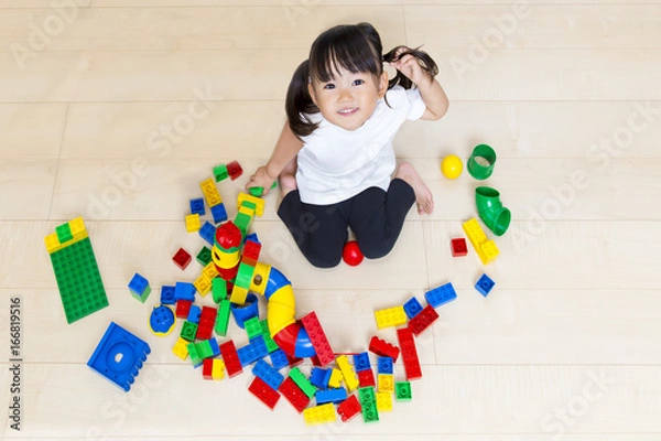 Fototapeta フローリングでブロック遊びをしながら見上げる幼い女の子
