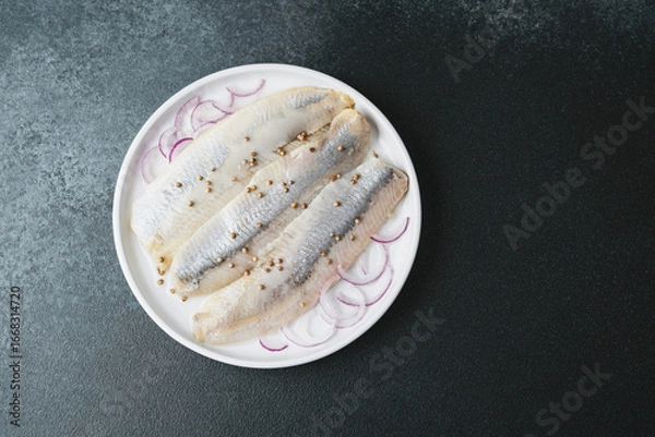 Fototapeta Marinated herring fillets with coriander seeds and onion on white plate over dark background