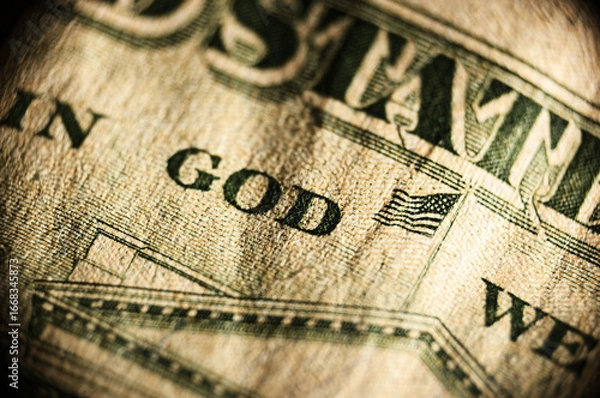 Fototapeta Showcases close-up of hundred dollar bill focusing on "IN GOD WE TRUST" text and small American flag graphic. Highlights green security strip and intricate patterns emphasizing worn, aged texture of