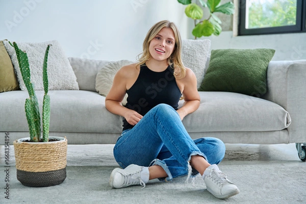 Fototapeta Portrait of relaxed beautiful young woman sitting at home on floor