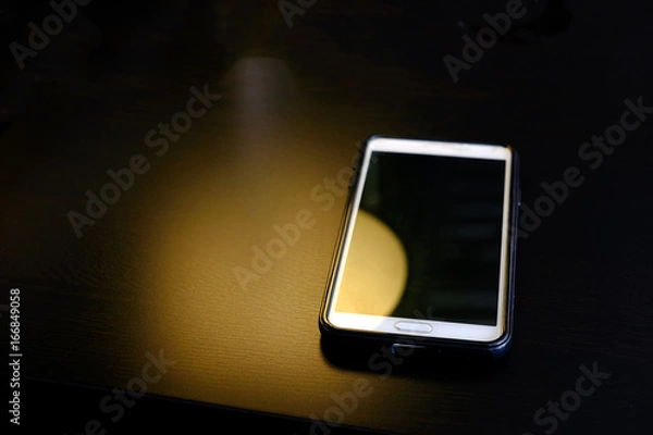 Fototapeta Abstract yellow light with smart phone on the table ,dark style
