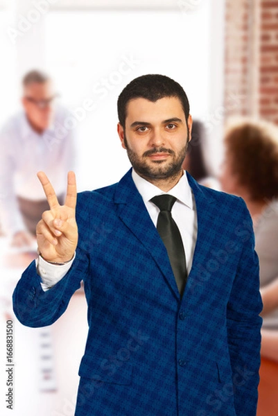Fototapeta Professional individual in business attire gesturing peace symbol, evoking positivity and confidence, set against a blurred office background representing teamwork and professional engagement.