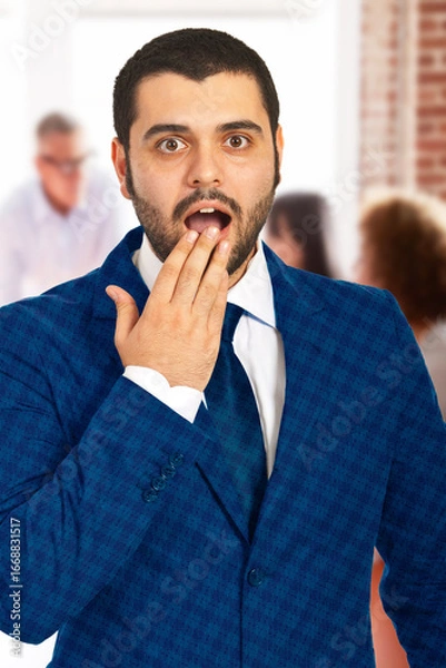 Fototapeta Shocked adult male in a blue suit, indoors with blurred people in the background. Expressing a surprised expression while wearing formal attire, reflecting emotional reaction and professional atmosphe