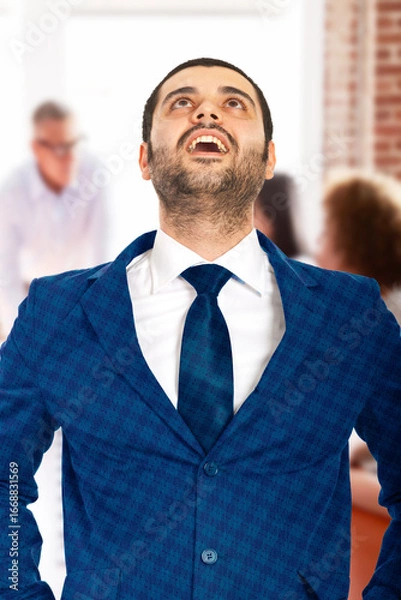 Obraz A professional man in a blue suit expresses joy and satisfaction in a dynamic office environment, highlighting success and accomplishment. The background shows a collaborative team working together, e
