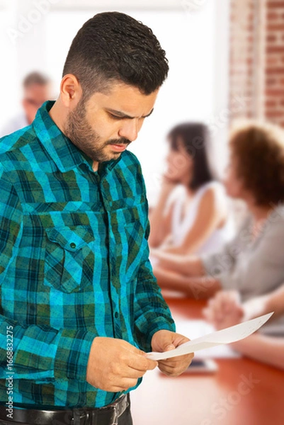 Fototapeta A man inspecting a document intently while colleagues engage in discussion at a table. The photo conveys a collaborative and professional atmosphere, symbolizing teamwork and focus within a workplace 