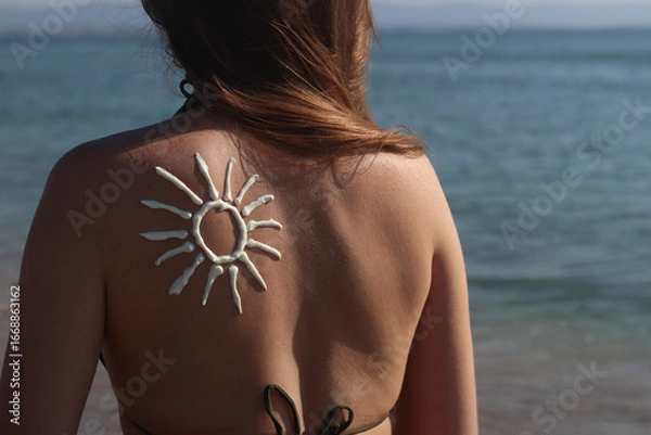 Fototapeta Sun image made with sunscreen on woman's back. Sunbathing on the beach. Close-up. Woman in swimsuit on the beach, back view. Using sunscreen. Concept of beach vacation, seaside resort, beach holiday
