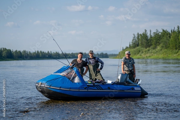 Fototapeta Three happy fishermen in a boat with spinning rods on a river near a forest