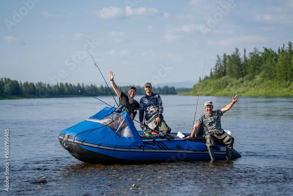 Fototapeta Three happy fishermen in a boat with spinning rods on a river