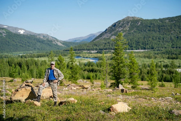 Fototapeta A hunter stands against the backdrop of a panorama of mountains and a forest 