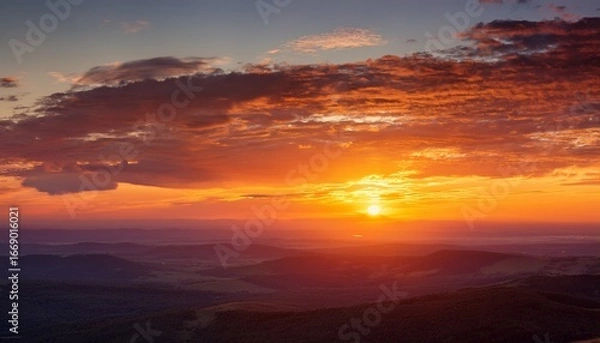 Fototapeta sunset glowing with warm hues blending soft cloudscape against serene landscape horizon