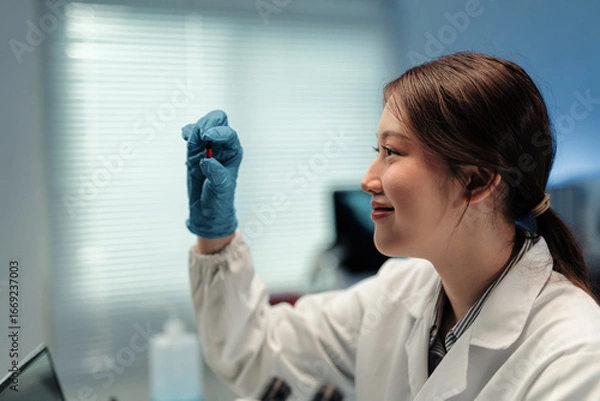 Fototapeta Smiling scientist examining a red and black capsule while conducting research in a modern medical laboratory filled with advanced equipment