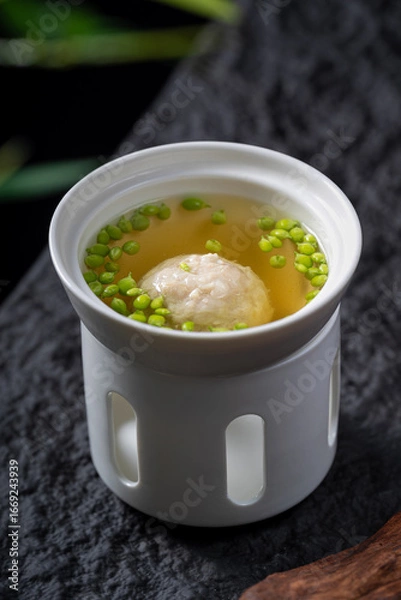 Fototapeta A bowl of soup with a meatball and green peas, served in a white container, looking very appetizing.