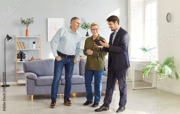 Fototapeta Male real estate agent or realtor guides a senior couple through a new property or apartment, assisting them in the home buying process. Focus is on finding the perfect new accommodation.