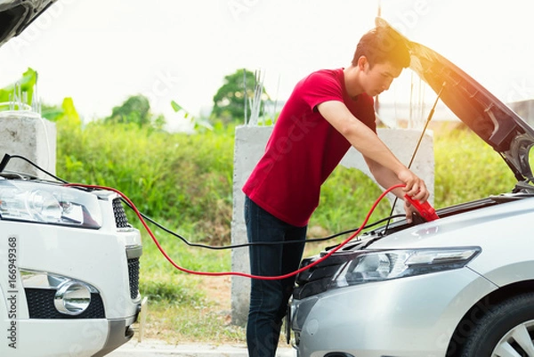 Fototapeta Man using jumper cables to start-up a car engine on the road.