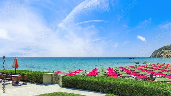 Fototapeta Stunning summer view from a seaside cafe terrace of a beautiful crowded beach with colorful red and green sun umbrellas on the Aegean coast, Halkidiki, Greece vacation travel background