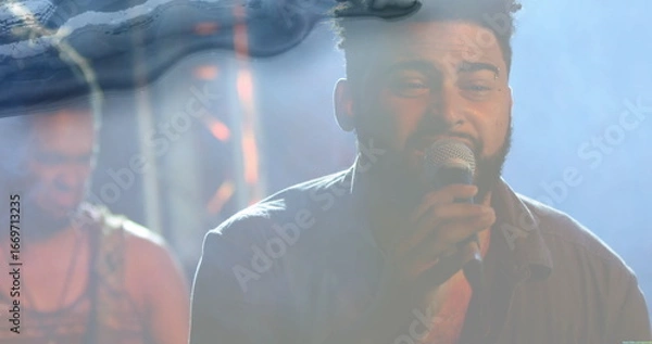 Fototapeta Singing bearded lead singer holding microphone on dimly lit stage, with foggy haze and metal truss