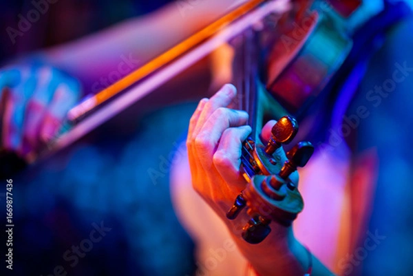 Obraz Close-up of woman hands playing violin under colorful stage lights