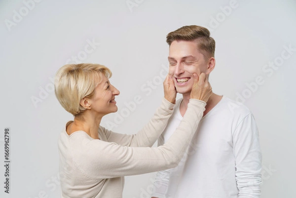 Fototapeta In a bright, inviting atmosphere, a mother playfully touches her adult son's face, bringing smiles and laughter to their heartfelt interaction as they cherish family togetherness.