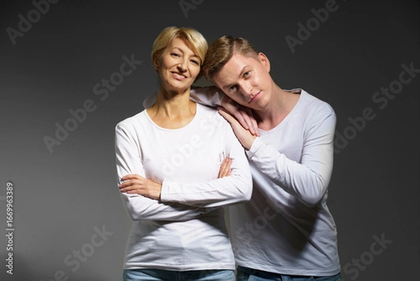 Fototapeta A mother smiles lovingly at her adult son, who leans playfully against her shoulder. Their expressions reflect closeness and joy, capturing a timeless moment of connection.