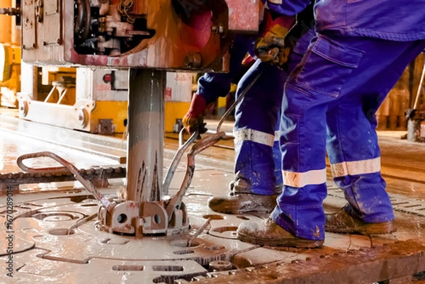 Fototapeta Driller's assistants near the drilling table on oil drilling platform soiled the overalls with drilling fluid.