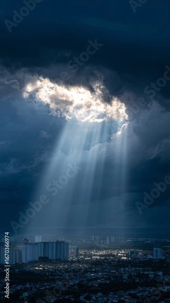 Fototapeta Sunlight streams through a break in the clouds, illuminating a city below with dramatic light.