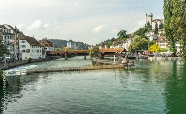 Fototapeta Panoramic photo of Lucerne from the Reuss River perspective, featuring the wooden Spreuer Bridge and the old tower, an element of the city's fortifications.
