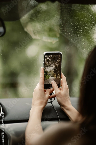 Fototapeta Person photographing a hanging bridge in lush tropical rainforest using a smartphone