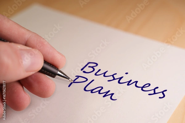 Fototapeta Hand holding pen writing business plan on a piece of paper. Suitable for images and concepts used by startups, financial consultants and entrepreneurship blogs.