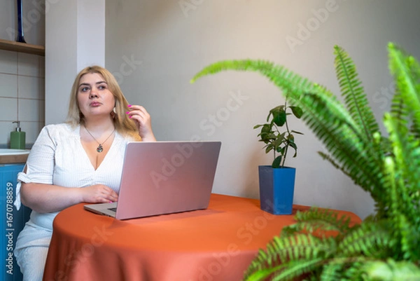 Fototapeta Plus size woman sitting at laptop looking distracted and tired. Burnout, procrastination, remote work fatigue, overthinking, emotional stress, mental exhaustion and lack of motivation concepts.