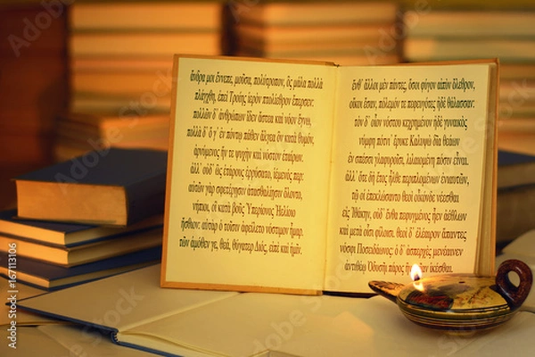 Obraz Open book illuminated by an oil lamp. The opening lines of The Odyssey written in the ancient Greek language. A stack of books. On the lamp, visible inscription Aphrodite in the Greek alphabet.