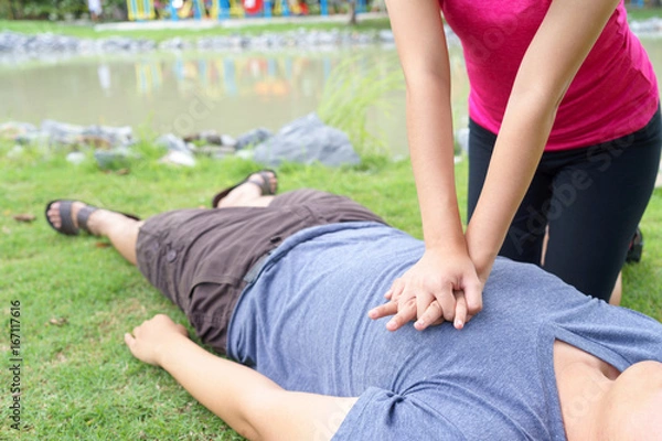 Obraz Woman giving cardiopulmonary resuscitation (CPR) to a man at public park.