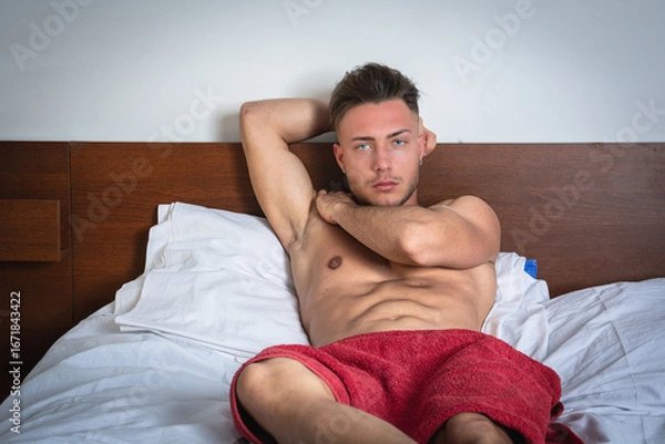 Fototapeta Young man relaxing on a bed with a red towel in a cozy room