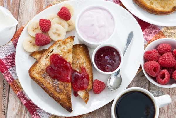 Fototapeta sweet toasts with fresh raspberry, jam and yoghurt for breakfast, top view