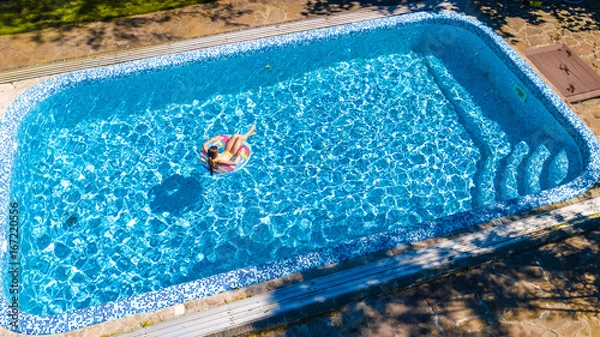 Fototapeta Aerial view of girl in swimming pool from above, kid swim on inflatable ring donut and has fun in water on family vacation
