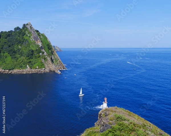 Fototapeta A sailboat rocks lazily at the mouth of Pasaia Bay on the waters of the Bay of Biscay in the Cantabrian Sea, Basque Country.