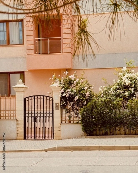 Fototapeta Cozy house with blooming roses near the gate, creating a charming and welcoming atmosphere.