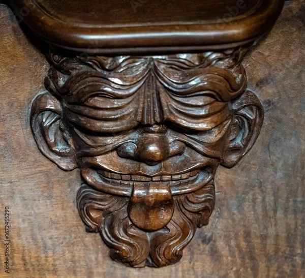 Fototapeta Old man with a beard sticking out his tongue - a funny and surprising wooden ornament from the wooden nobles' seat from the cathedral in Basel	