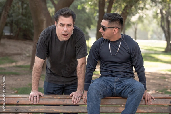 Fototapeta Two men in a park, one looking surprised, the other wearing sunglasses.