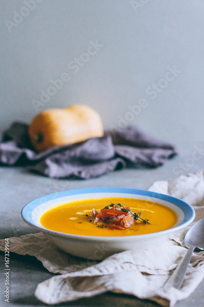 Fototapeta A plate of pumpkin soup with a jamon, garlic, thyme and cream, on a gray background