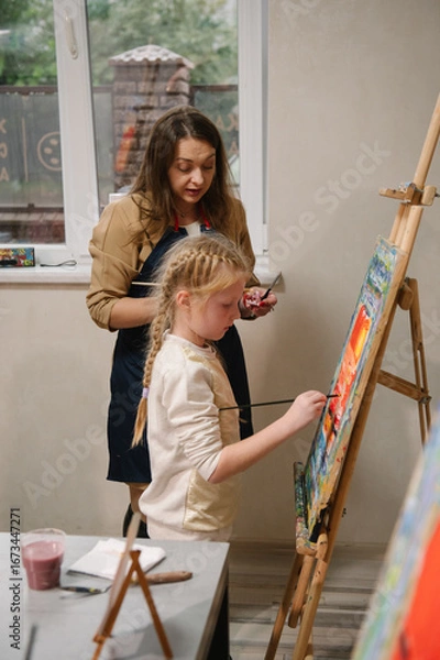 Fototapeta Teacher learn children to draw pictures in an art lesson. Artist explains how to mix and combine colors. Childs painting in workshop. Kids drawing brush on easel. Education, learning concept.