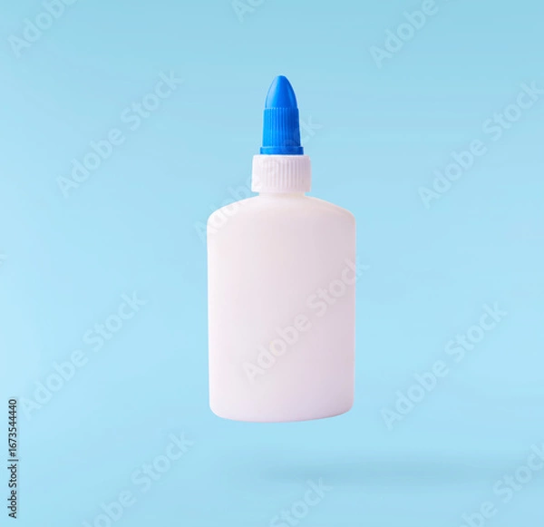 Fototapeta Back to school conception. Flying in the air school equipment. A PVA glue bottle levitating in the air isolated on blue background