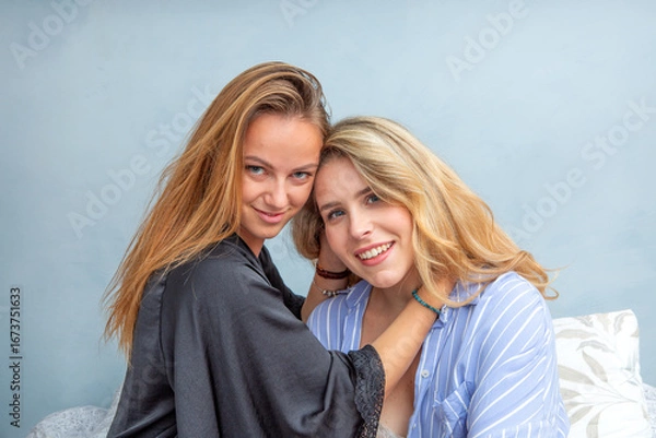 Fototapeta Lesbian couple smiling and embracing while looking at camera indoors