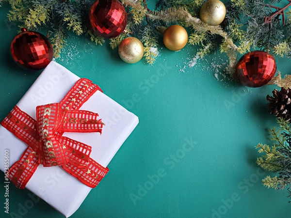 Fototapeta white gift with red ribbon and gold and red Christmas ornaments on a green background with space for text