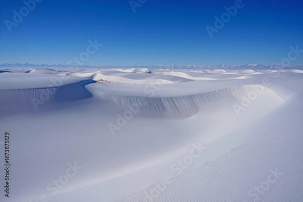 Fototapeta Vast frozen desert landscape under a clear blue sky with rolling snow dunes