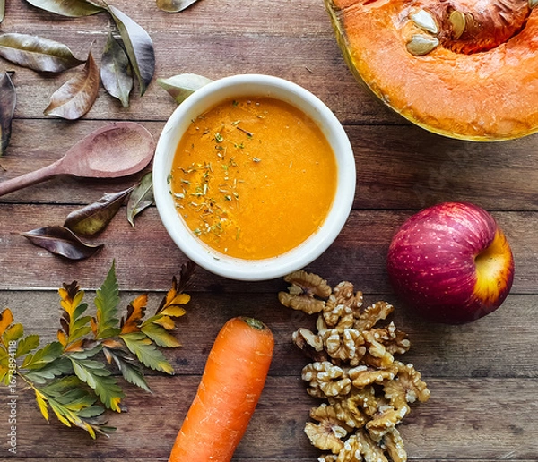 Fototapeta 
table with leaves and autumn foods such as pumpkin and carrot cream and spices, apple, nuts on wooden background