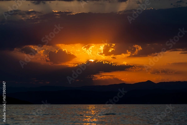 Fototapeta Golden Sunset Over Silhouetted Mountains and Tranquil Waters