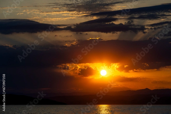 Fototapeta Golden Sunset Over Silhouetted Mountains and Tranquil Waters